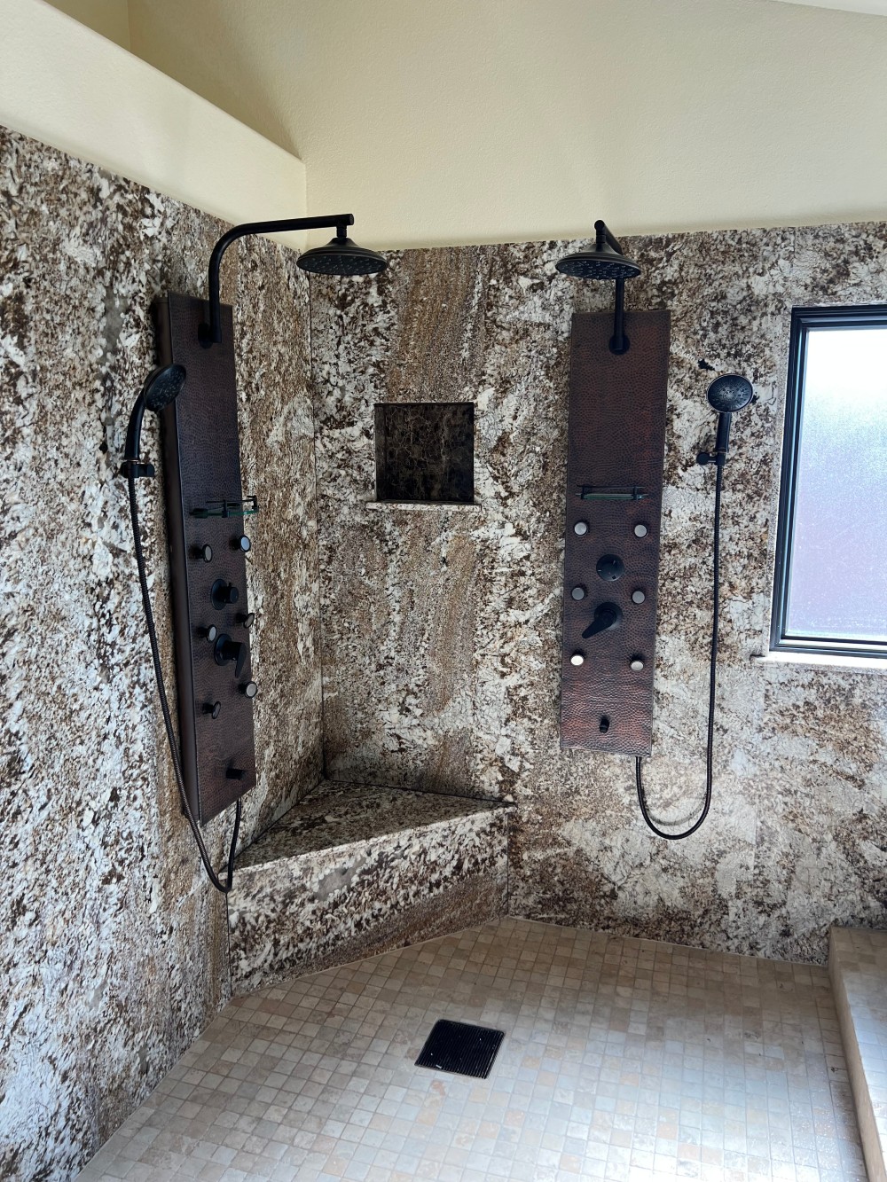 Custom walk-in shower with dual rainfall shower heads and travertine walls plumbed by Omnia Plumbing.
