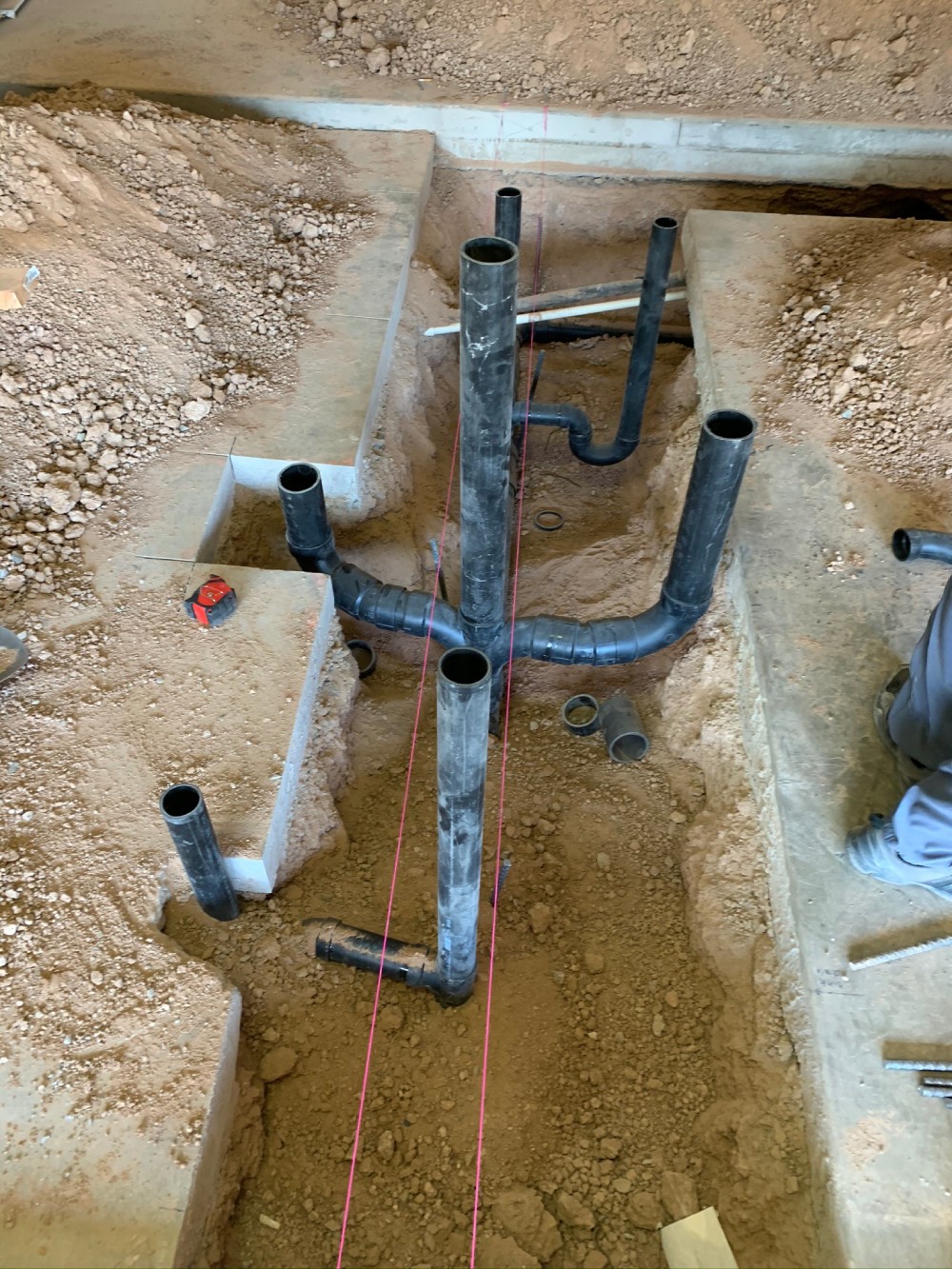 ABS drain, waste, and vent rough-in with multiple stub-ups installed in a trench by Omnia Plumbing.