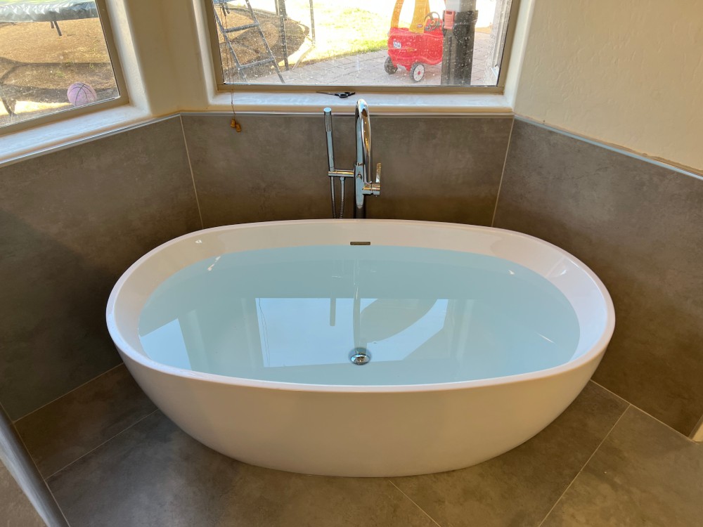 Finished freestanding white acrylic soaking tub with floor-mounted filler installed by Omnia Plumbing.